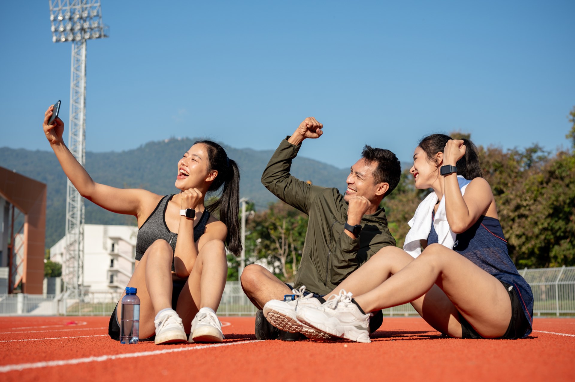 Three friends sitting on an athletics track after a run, cheering