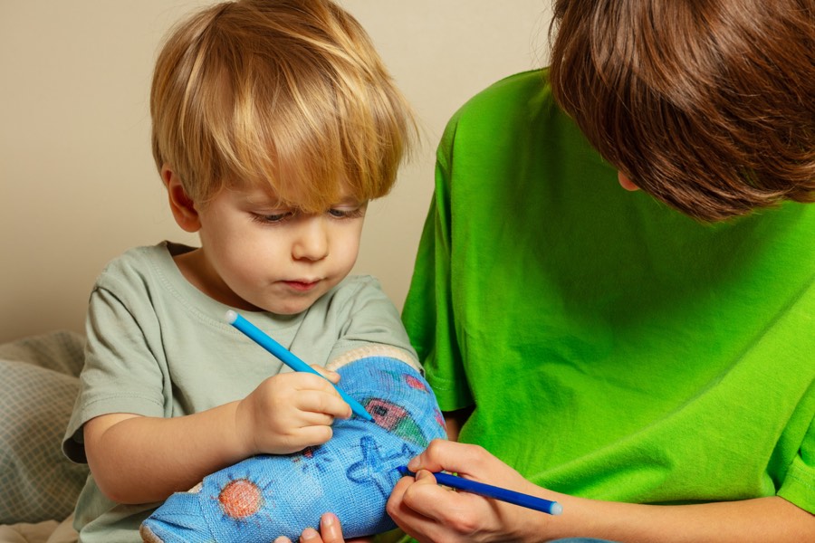 Child drawing on their arm cast