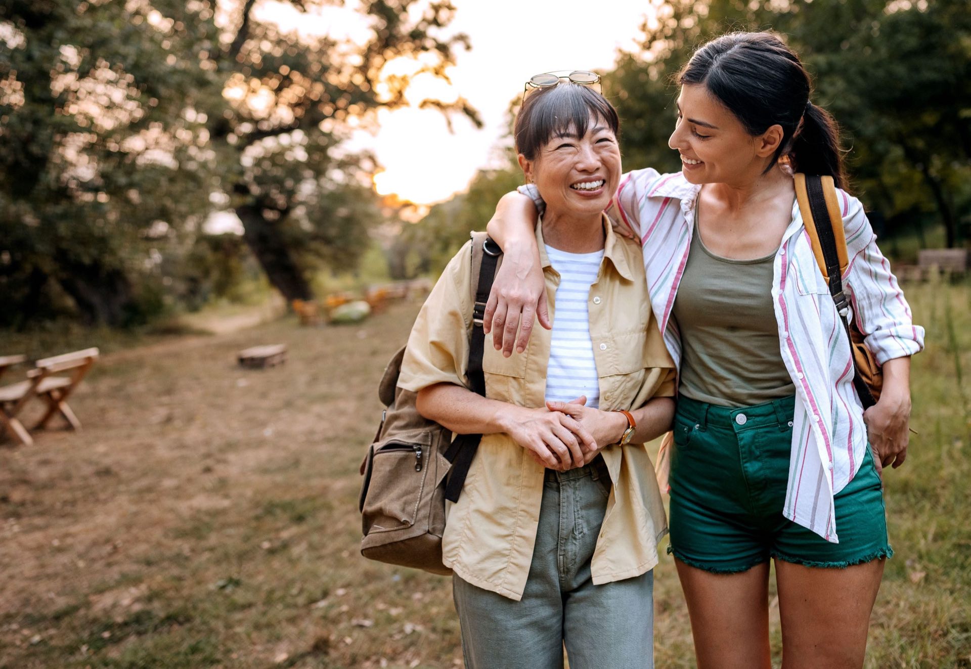 Two women walking arm in arm along a bush trail at sunset