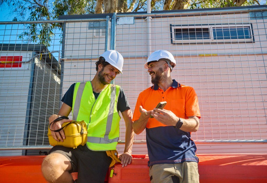 Two tradespeople on site, laughing over a phone